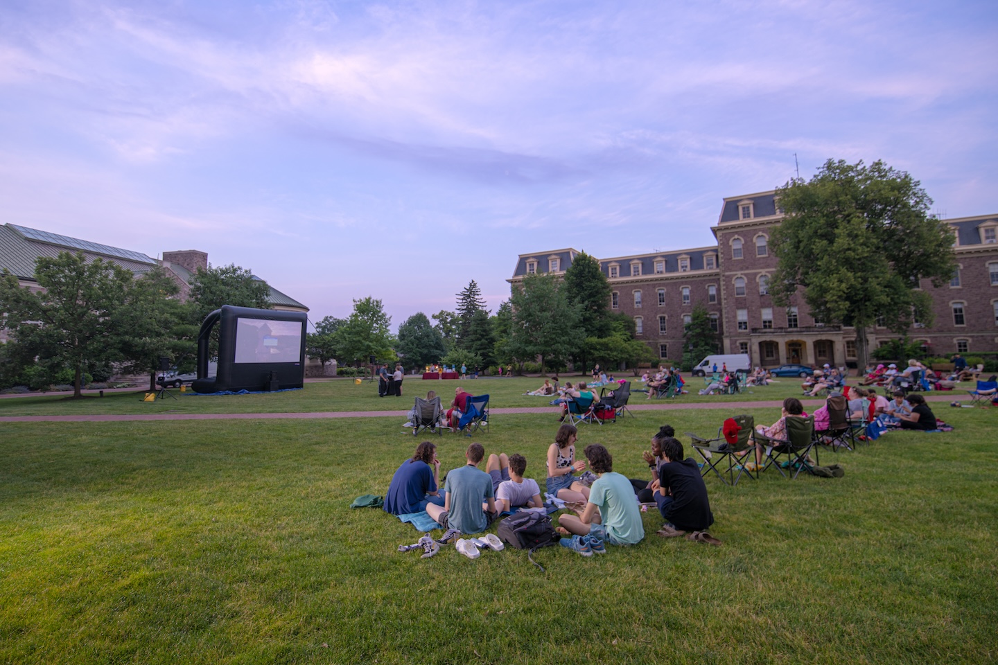 Students, staff, faculty, and neighbors sit on the grassy Quad looking at a large blow up screen in front of Farinon during Movies on the Quad.