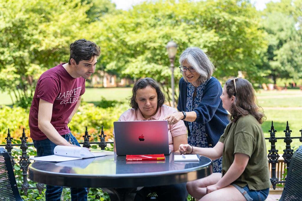 Bianca Falbo, Emma Hetrick, Ethan Eisenberg '28, and Jessi Kleiber '27 sitting at a table outdoors on Lafayette campus discussing their research project on the history of the College Writing Program