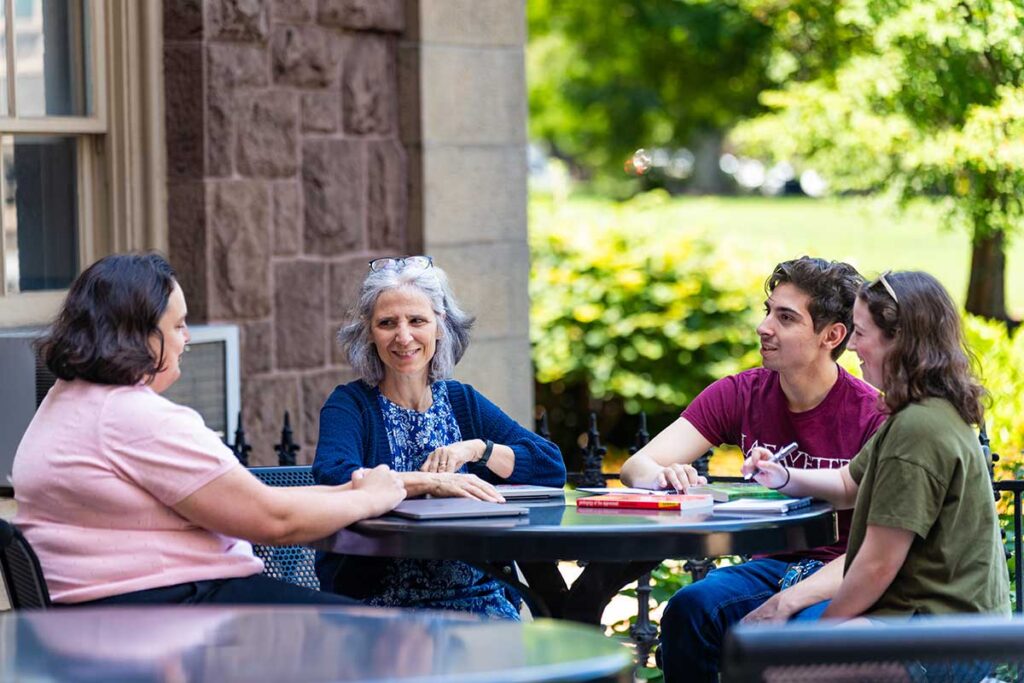 Bianca Falbo, Emma Hetrick, Ethan Eisenberg '28, and Jessi Kleiber '27 sitting at a table outdoors on Lafayette campus discussing their research project on the history of the College Writing Program