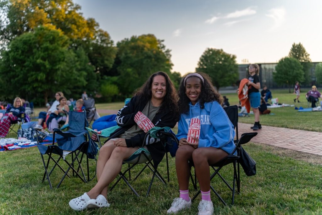 A mom and daughter sit on chairs on the Quad for Movies on the Quad.