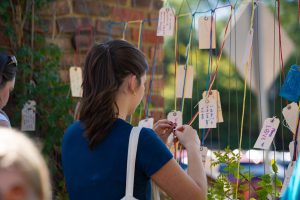 A visitor to the 2025 Community Arts Fair hangs a line of custom prose on a colorful string as part of the fair.