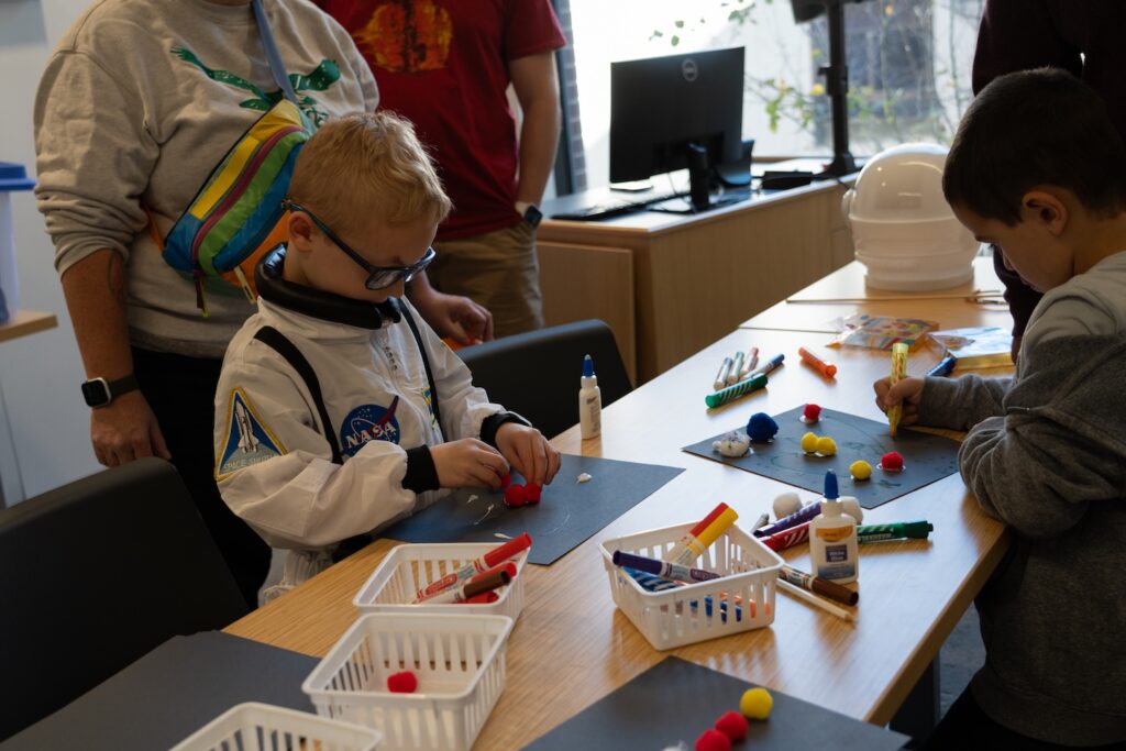 A young boy in an astronaut outfit works on a craft during Space Fest