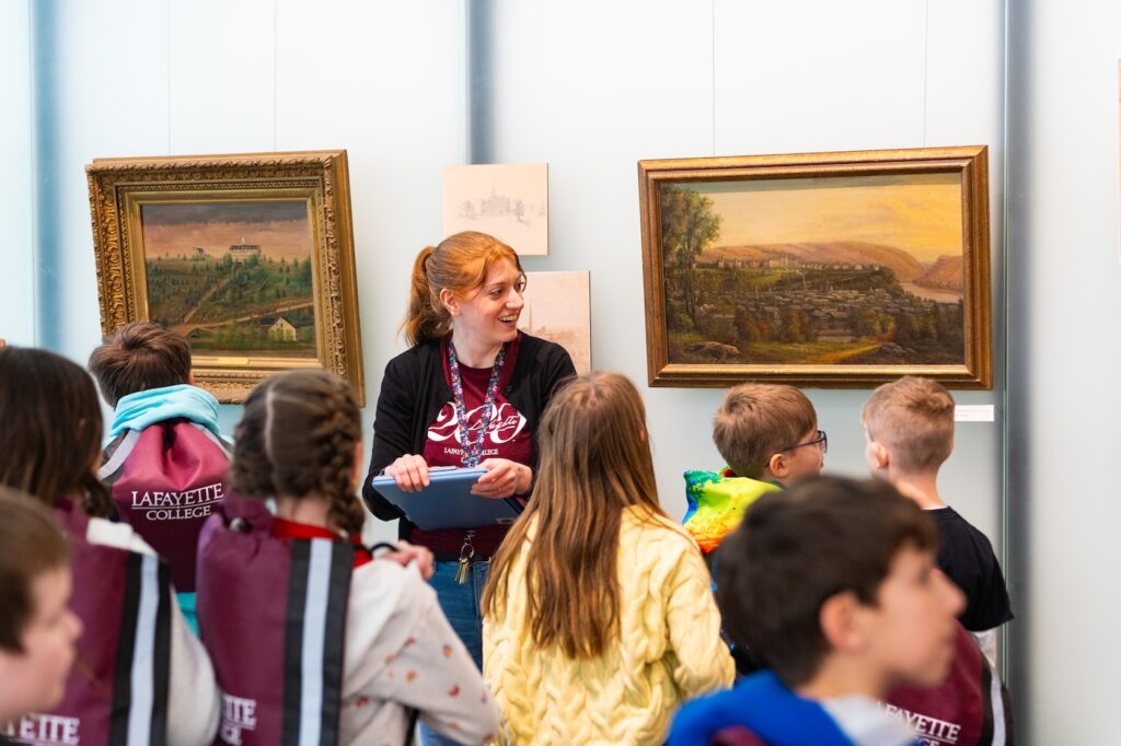 Missy Nerino stands near two paintings of early Lafayette College and explains the history to a group of fourth graders
