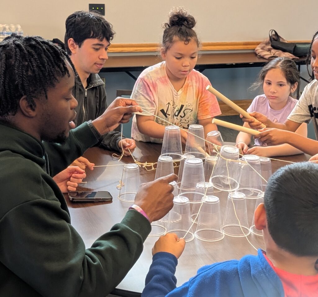 Lafayette students in Connected Classrooms sit at a table with EASD students as they build a structure out of plastic cups and skewers.