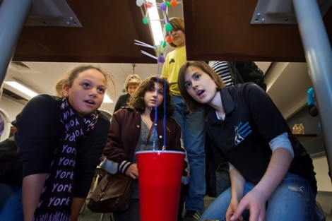 Students watch as Emily Crossette '15, right, puts their bridge through the weight test. 