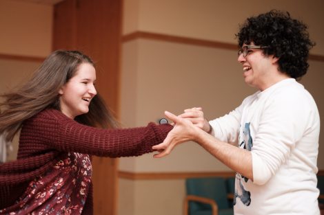 A male student and female student laugh as they do salsa dancing together.