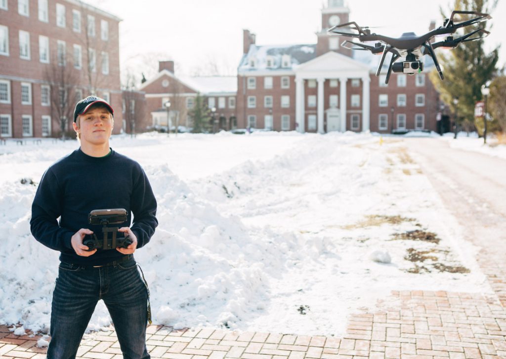 Travis Shoemaker '18 holds the remote control for a drone that flies overhead.