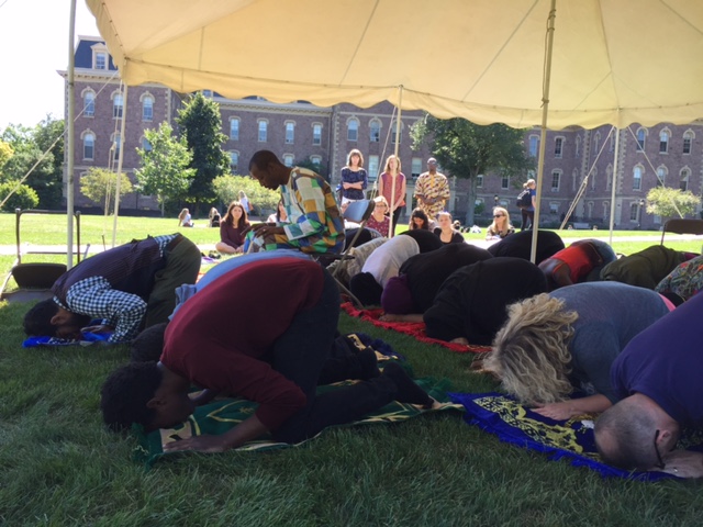 Students, faculty, and staff bow in Muslim prayer under a tent on the Quad.