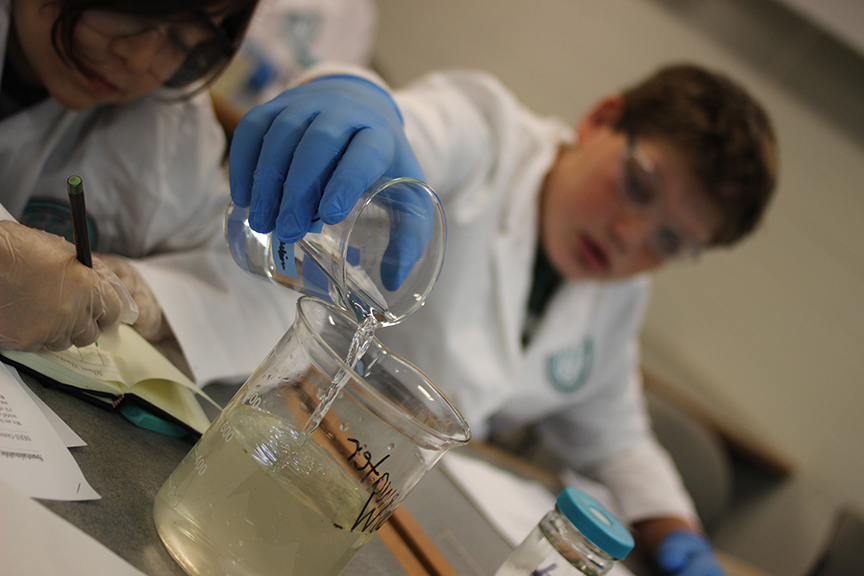 A middle school boy pours liquid into a beaker.