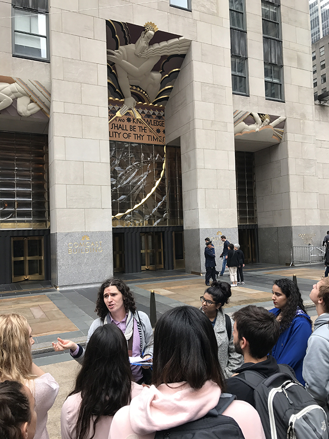 the class listens to a lecture while viewing a Rockefeller relief outdoors in New York City.