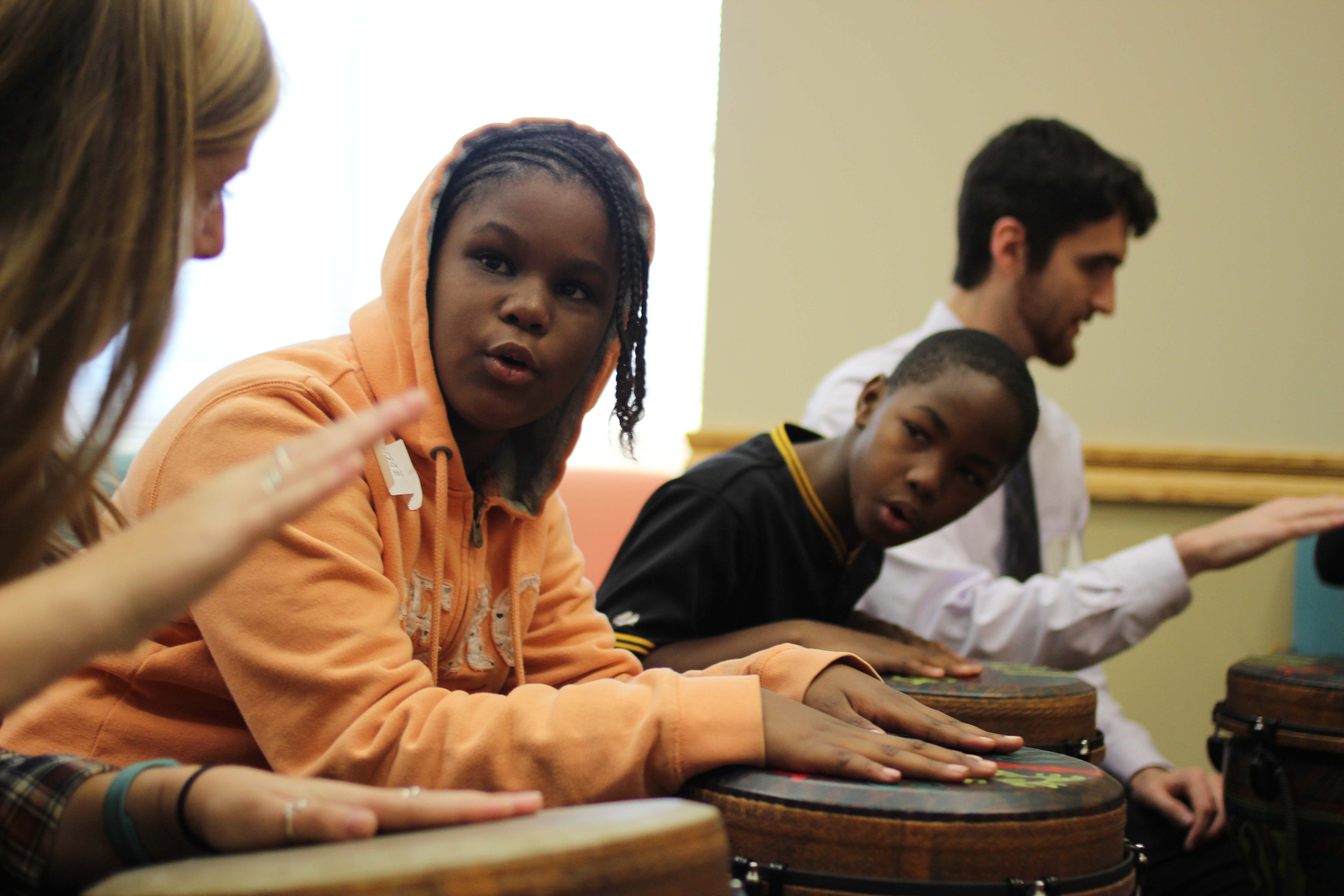 Two young children and two Lafayette students drum in class.