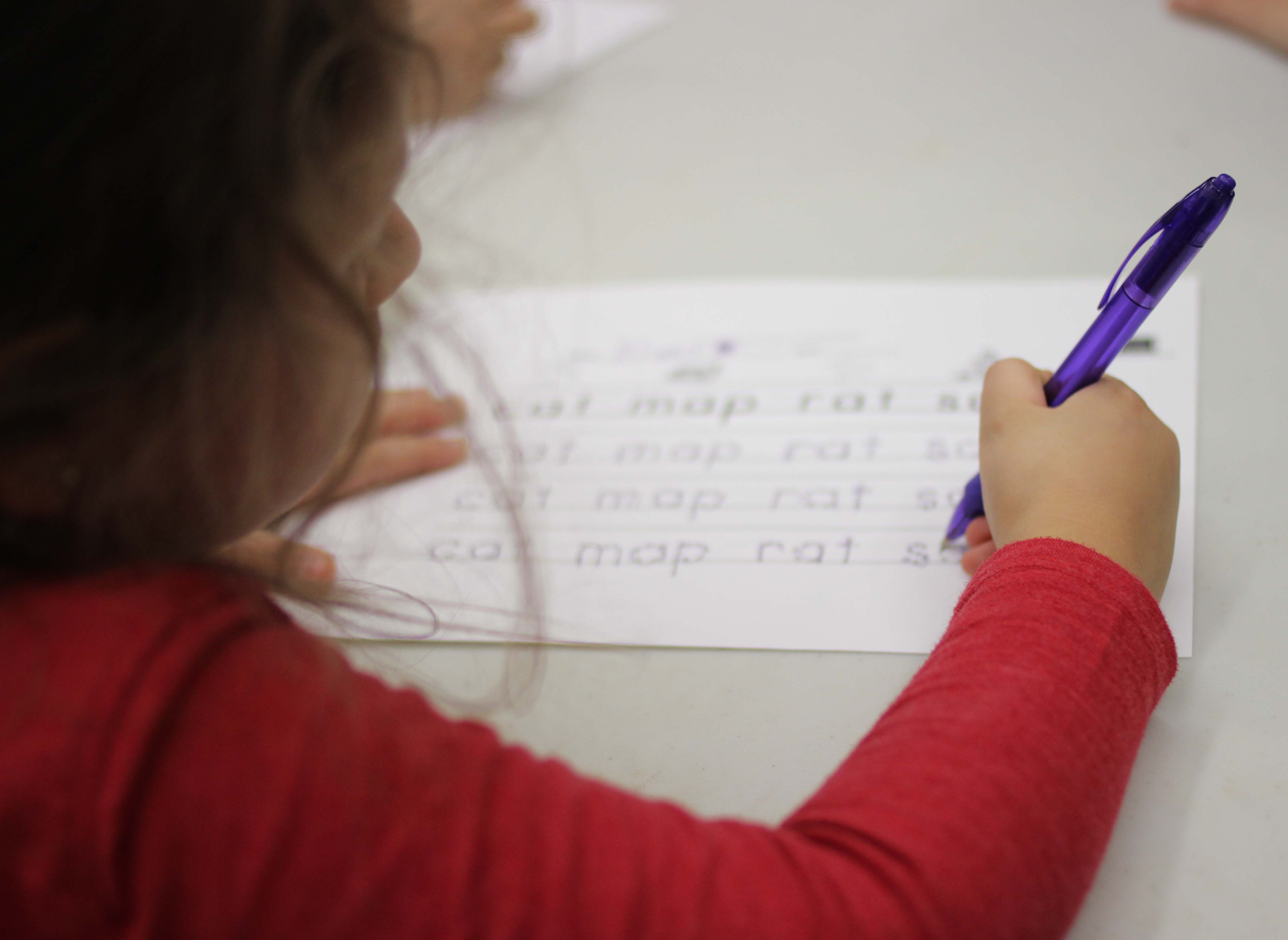 A young girl traces letters on paper.