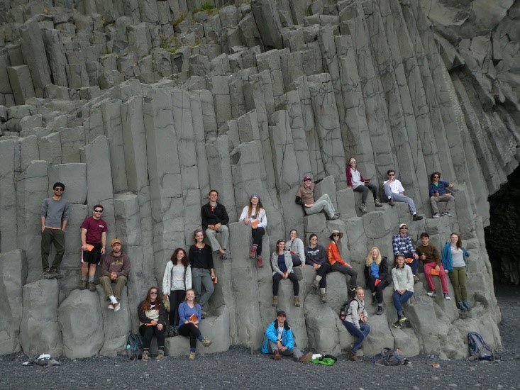 Students sit upon lava formations and columns that formed at Reynisfjara Black Sand Beach.