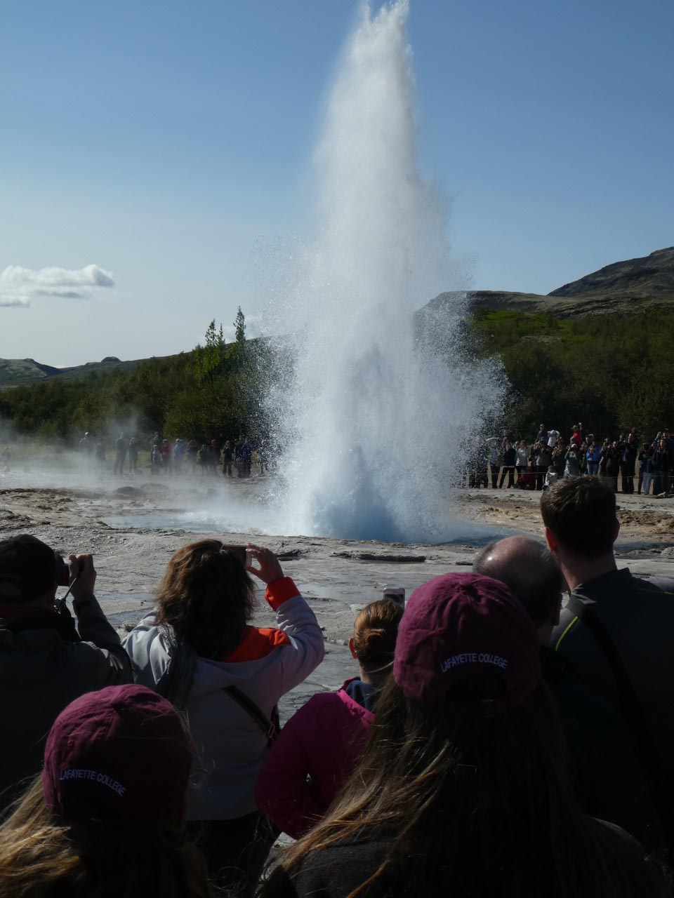 Students watching a geyser called Strokkur erupt water and steam in Iceland