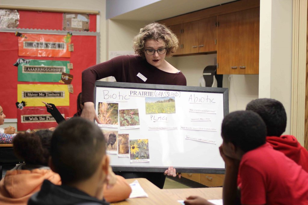 A female Lafayette student holds up a visual aid about prairies.