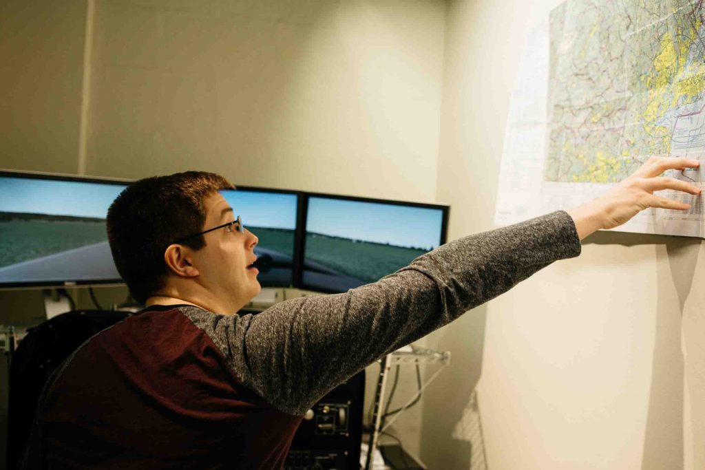 A student checks a map hanging on the wall to the right of the flight simulator.