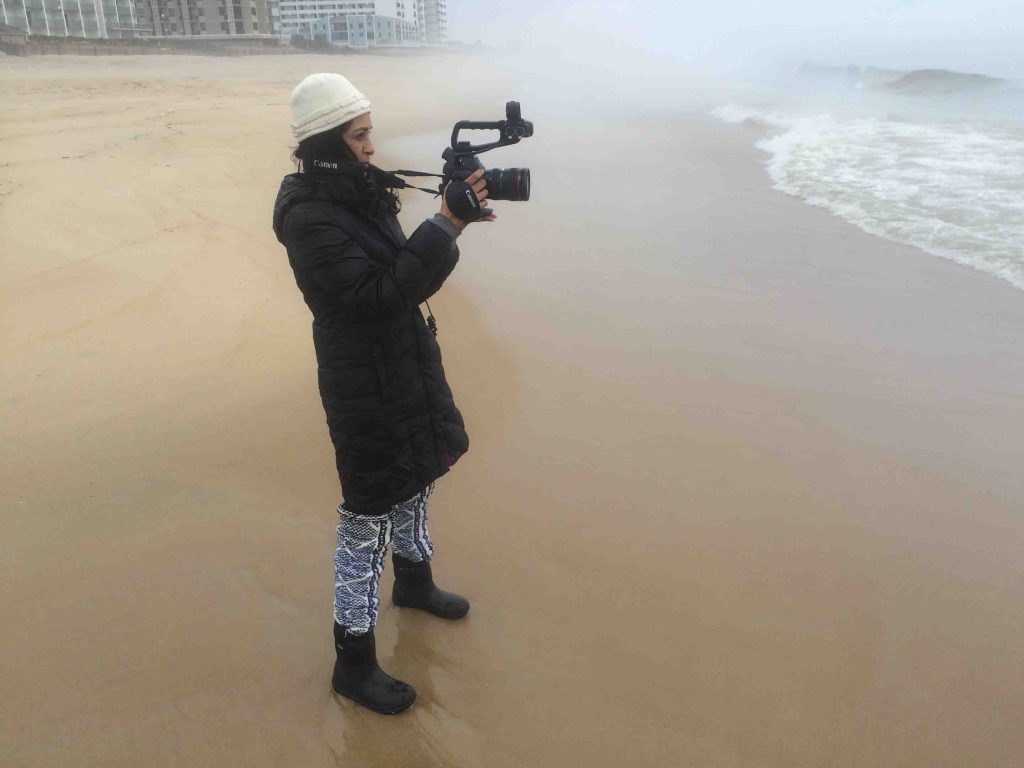 Film and media studies professor Nandini Sikand films the water on a beach.