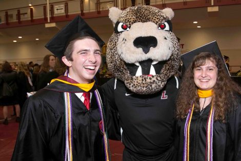 Two grads smile with the Leopard after Commencement.