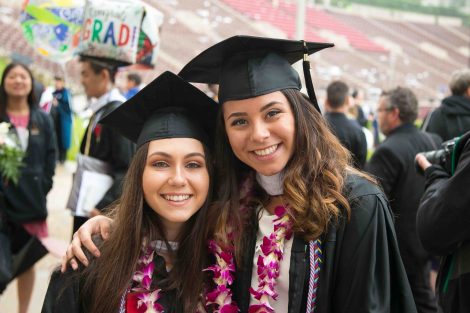 Two women graduates smile and pose after Commencement.