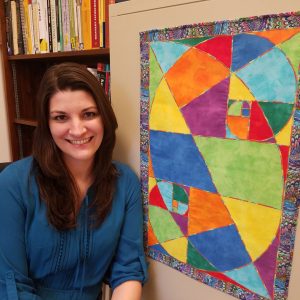 Allison Lewis stand by a quilt she made that has two Fibonacci spirals.