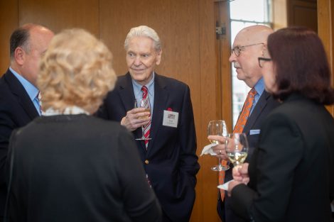 Larkin Professor Emeritus Joseph Sherma holds a glass of wine while listening in a group of five people standing at the Societe d'Honneur dinner