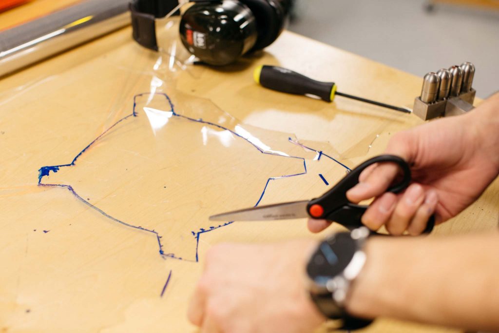 A student uses scizzors to cut plastic in the mechanical engineering lab.