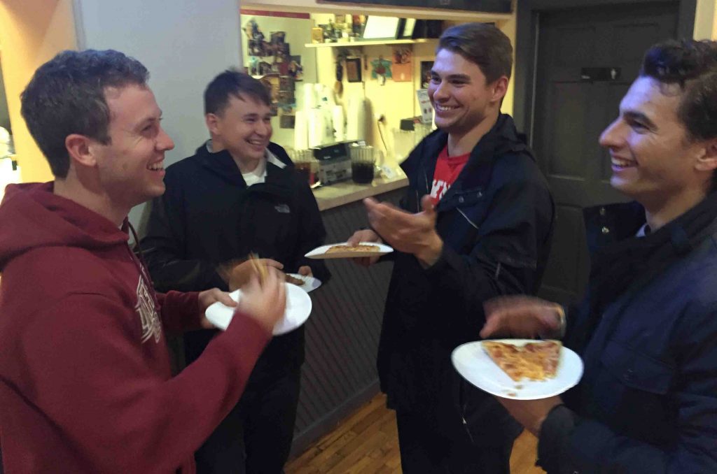 Four men students eat pizza while talking and laughing on Election Night in Campus Pizza.