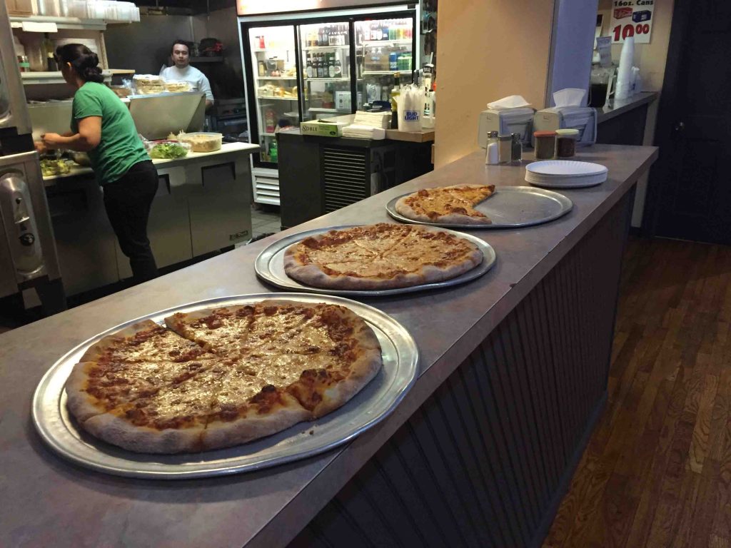 Three pizzas sit on the counter of Campus Pizza.