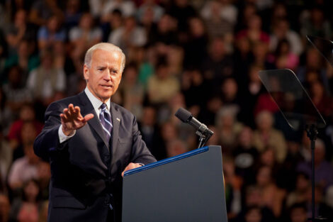 Joe Biden speaks from a podium. A crowd of people can be seen behind him.