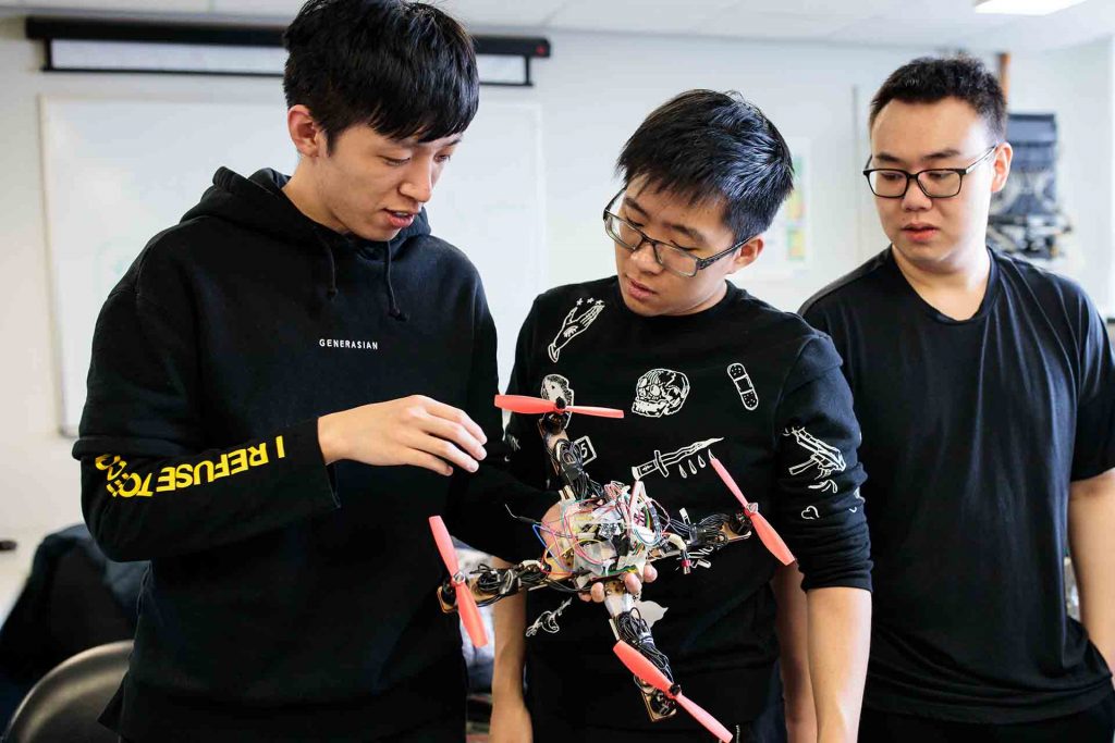 Three male students inspect the drone they built.