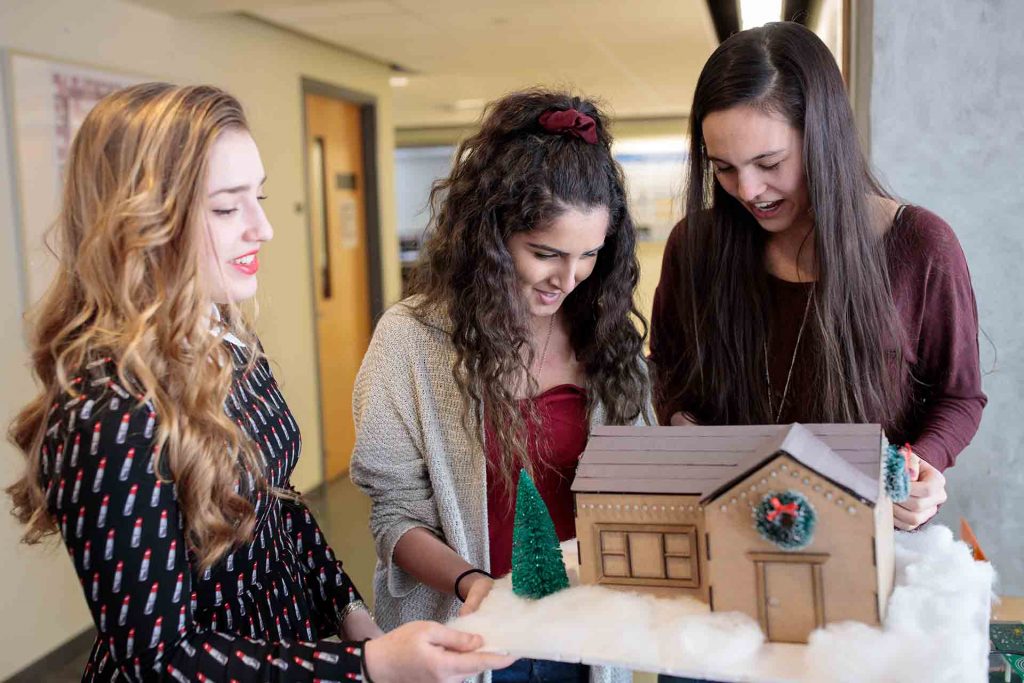 Three female students gather around the house model they constructed.