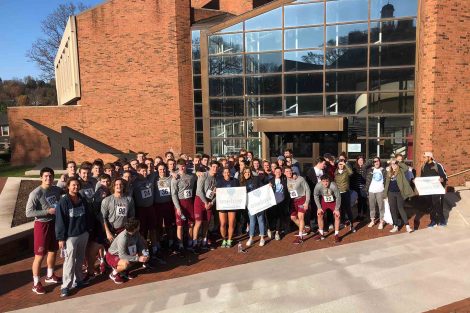 Team members pose outside the Williams Center for the Arts with banners for the One Love 5k run.