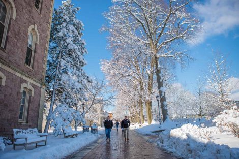 Students walk on a brick walkway in front of Pardee Hall after snowfall.