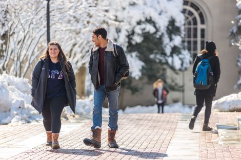 Students walk and talk together on a brick walkway with Colton Chapel in the background following snowfall.