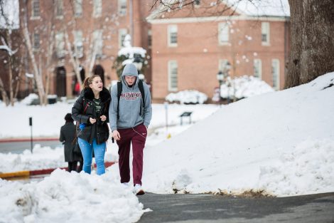 Two students talk and walk on campus after snowfall.