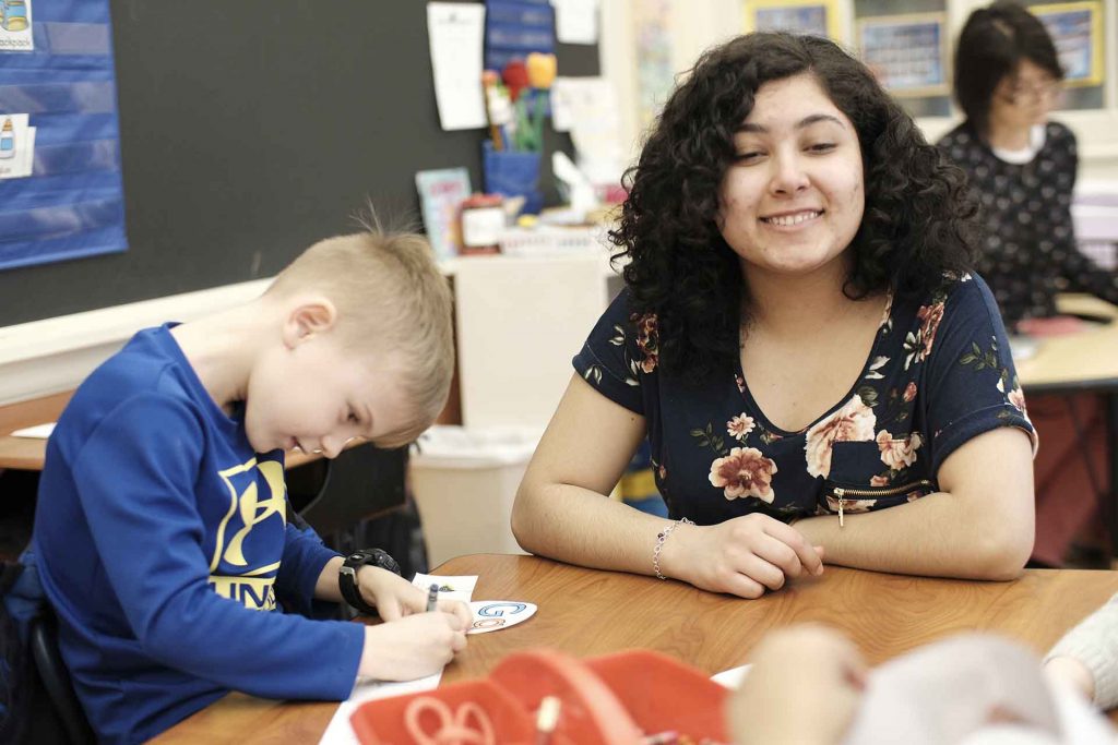 Lafayette student smiles as she works at a table with kindergartners.