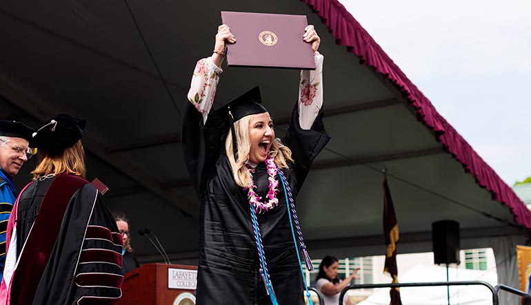 Mailinda Hoxha '19 holds up her degree at Commencement and smiles