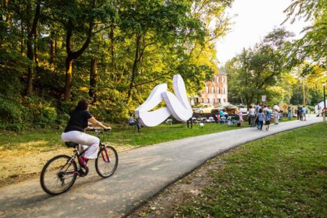 Bicycle heads toward a giant pair of white wings, a sculpture on the Karl Stirner Arts Trail