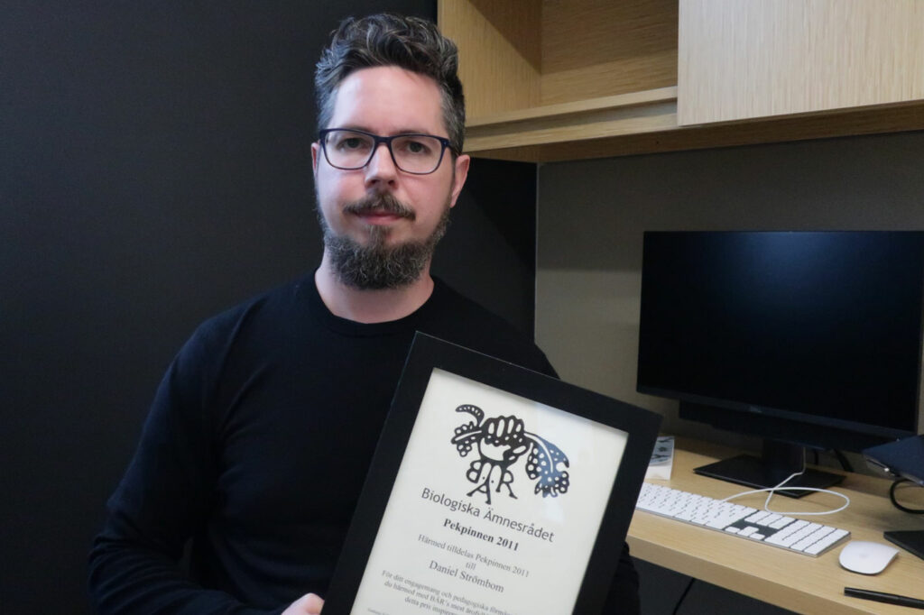 Daniel Strömbom holds a framed certificate for a teaching award given to him by biology students.