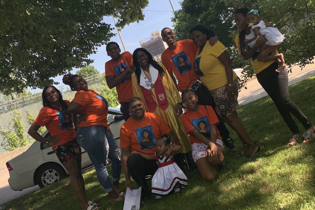 Omayra Henriquez surrounded by her family at her high school graduation. All wear bright t-shirts with her face on the front.