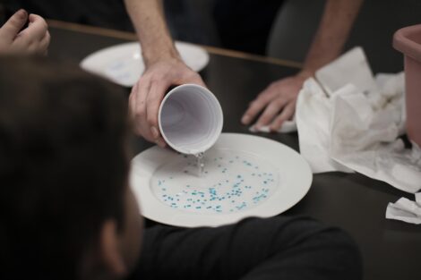 Student pours water on maker dots on white plate