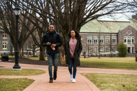 Two friends talk with walking on a brick pathway on the Quad on the first day of spring semester.