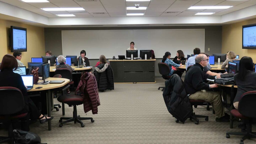 Faculty sit at computers and receive instruction from IT staff