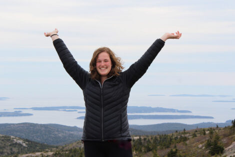 Liz Rohricht has her arms lifted above her head with a scenic, water backdrop