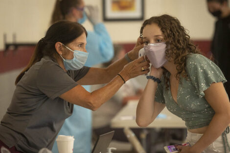 A masked healthcare worker gives a masked student a temperature check.