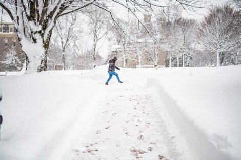 A student crosses a snow-covered path in the Quad