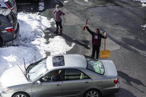 A student holds shovels while helping a vehicle get out of its parking spot
