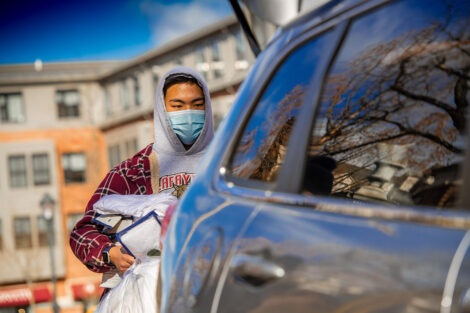 A masked students takes items out of the trunk of a vehicle.