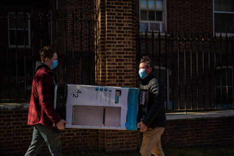 A masked student carries a refrigerator box with their family member