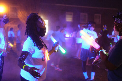 students dance at night wearing masks and holding glow sticks